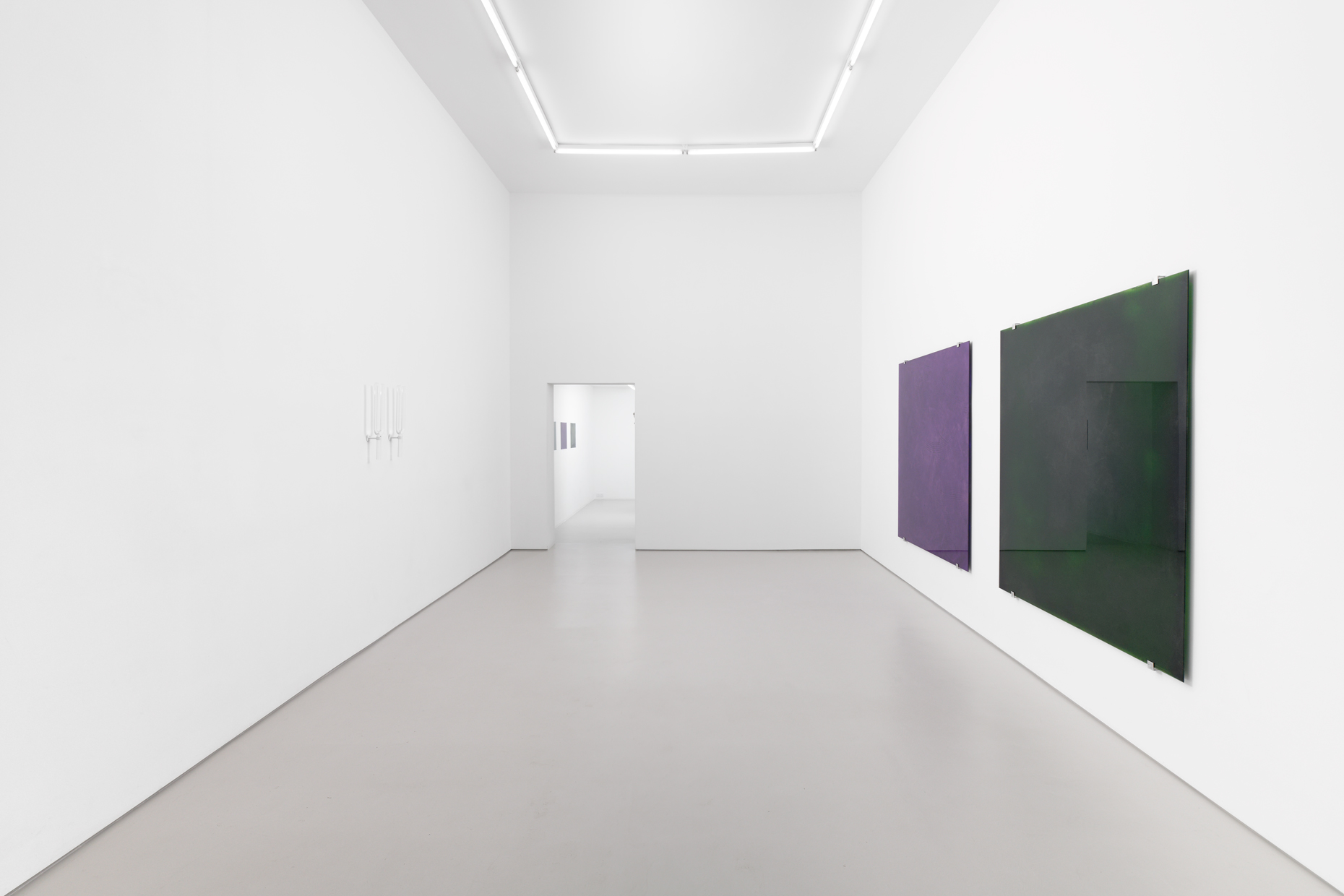 two glass tuning forks on the left wall facing two glass paintings, one purple the other dark green on the right wall.
